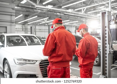 Two Auto Mechanics In Red Uniform Standing Together In Front Of The Luxury Car At The Car Service