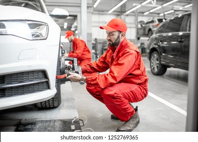 Two Auto Mechanics In Red Uniform Fixing Disk For Wheel Alignment On A Luxury Car At The Car Service