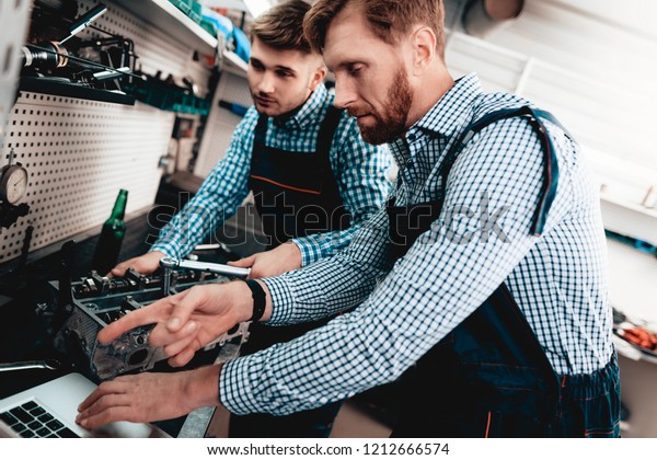 Two\
Auto Mechanics Work Together In Garage. Wrench Using. Laptop Screen\
Staring. Information Sharing. Professional Uniform. Confident\
Engineering Specialist Team. Service Station\
Concept.