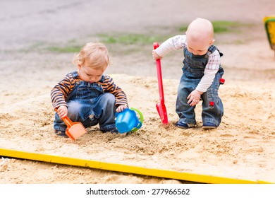 Two Baby Boys Playing With Sand In A Sandbox