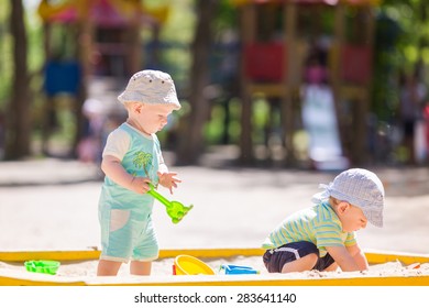 Two Baby Boys Playing With Sand In A Sandbox