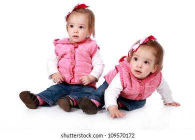 Two Baby Girl Identical Twins Wearing Blue Jeans And White Top With Pink Gillet And Wearing Red And White Polka Dot Ribbon Bows In Their Hair Looking Cute And Adorable On A White Seamless Background