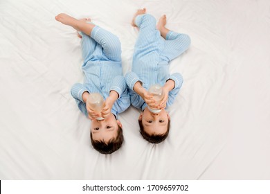 Two baby twin boys in pajamas lie on the bed drinking milk from bottles. View from above. concept of marriage and friendship. concept of baby food.space for text