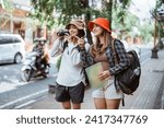 two backpacker girls walk to find a tourist destination carrying a camera and map on the roadside