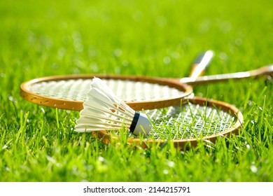 Two badminton rackets and a shuttlecock lie on the green grass. Outdoor recreation and fresh air. The sun's rays. Lawn for playing badminton. - Shutterstock ID 2144215791