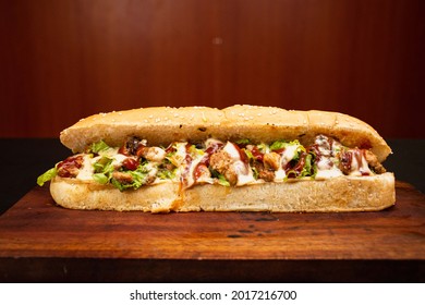 Two baguette sandwiches or Submarine sandwiches with toasted chicken, vegetables, cheese, lettuce, sweet sauce, mayo,  onion, and fresh french fries cutting board. Long subway on a dark background.