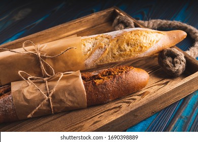 Two baguettes of wheat and rye flour on a tray on a blue wooden background.