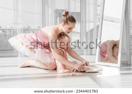 Two ballerinas, mother and daughter sitting on the twine in front of large windows in studio. Little ballerina girl and her teacher doing the split. Little girl stretching with her mother