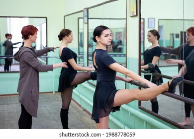 Two Ballerinas Training In A Studio With Teacher. Warming And Stretching Near Barre In Front Of Big Mirrors, Becoming Better Dancers.