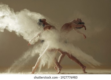 Two ballet dancers perform dance on the floor covered flour against background of white flour cloud in air.