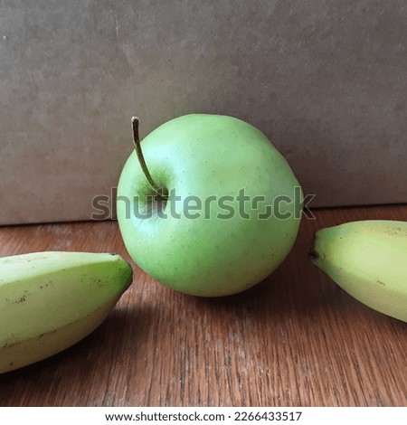 Two bananas pointing at an apple.Wood surface and lightbrown background.