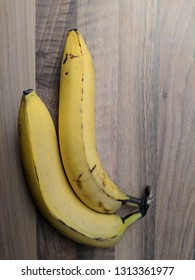 Two Bananas In Stark Lighting On A Wooden Table