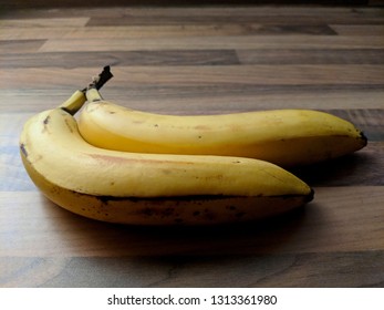 Two Bananas In Stark Lighting On A Wooden Table