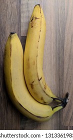 Two Bananas In Stark Lighting On A Wooden Table