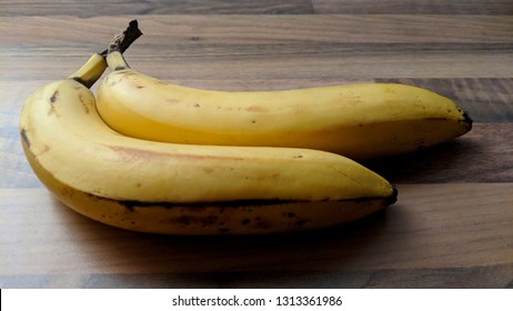 Two Bananas In Stark Lighting On A Wooden Table