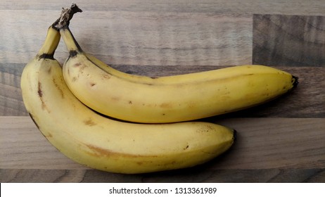 Two Bananas In Stark Lighting On A Wooden Table