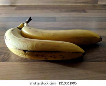 Two Bananas In Stark Lighting On A Wooden Table