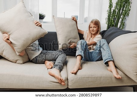 Two barefoot children having fun with pillows on a cozy sofa in a bright living room, enjoying playful moments and sibling interaction at home.