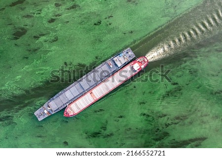 Two barges loaded with grain are sailing down the river to a commercial port for unloading. Aerial view.