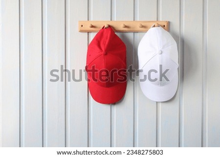 two baseball caps, red and white, hang on a wooden hanger on the board wall. summer headdress, hat, cap.