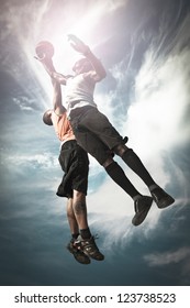 Two Basketball players playing street basket and jumping together to catch the ball