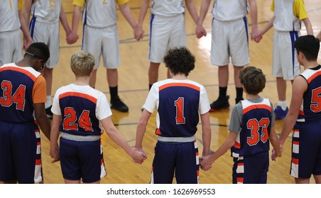 two basketball teams hold hands during a pregame prayer.