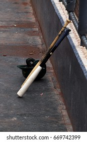 Two bats leaning against the outside wall of a dugout in front of a batting helmet