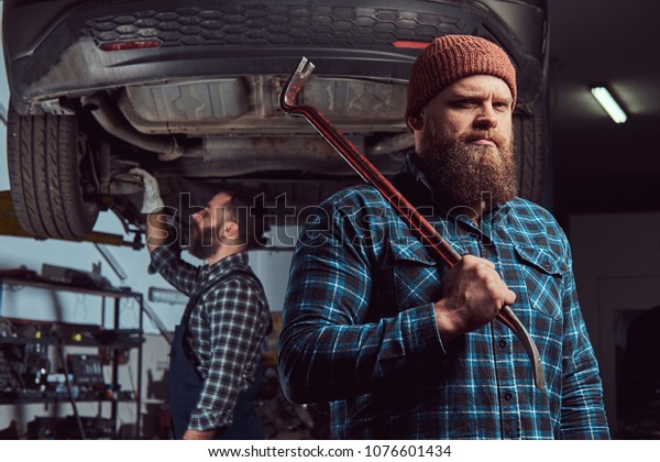 Two bearded brutal mechanics repair a car on a lift in\
the garage. 