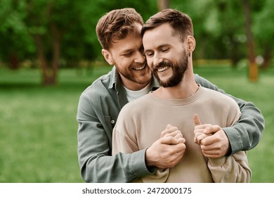 Two bearded men, a gay couple, hold hands and laugh in a lush green park. - Powered by Shutterstock