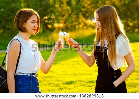 two beautifu best girlfriends schoolgirls ( student) eating ice cream in a waffle horn in the park