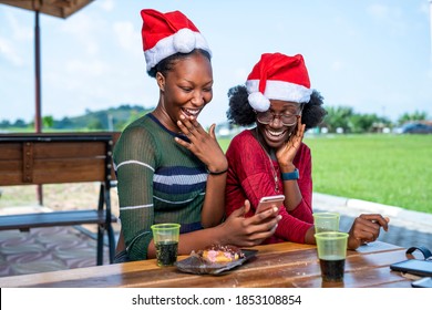 Two beautiful African American women celebrating Christmas outdoor-feeling happy looking at phone-black people making video call in festive season during covid-19 pandemic - Powered by Shutterstock