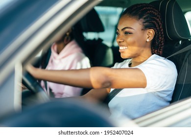 Two beautiful african young cheerful women looking at each other with smile while sitting in car