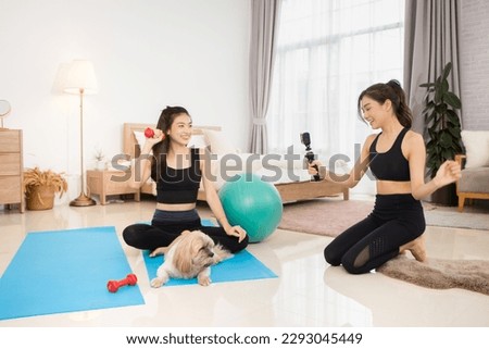 Two beautiful Asian girls wearing workout clothes and smiling with dogs in bedroom. woman on exercise mat with dumbbells and tablet
