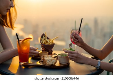 Two beautiful Asian woman friends meeting and dinner party together at skyscraper rooftop restaurant in metropolis at summer sunset. Female friend enjoy outdoor lifestyle activity in the city at night