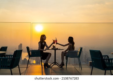 Two beautiful Asian woman friends meeting and dinner party together at skyscraper rooftop restaurant in metropolis at summer sunset. Female friend enjoy outdoor lifestyle activity in the city at night - Shutterstock ID 2108767283