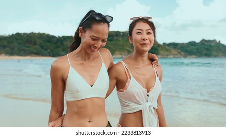 Two beautiful Asian women in bikini walking and talking relaxing on the beach in a tropical island on summer. The happiness and friendship of friends during travel and tourism. - Shutterstock ID 2233813913
