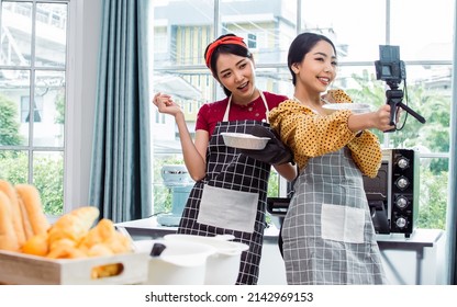 Two Beautiful Asian Women Cooking Food, Making Bread For Breakfast And Bakery While Using Tablet, Streaming Live Video Clip Or Taking Selfie Photo Together With Happiness And Fun In Kitchen At Home