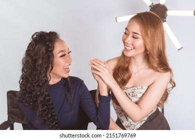 Two beautiful asian women having fun on a photoshoot set while waiting. Isolated on a white background. - Shutterstock ID 2151769769