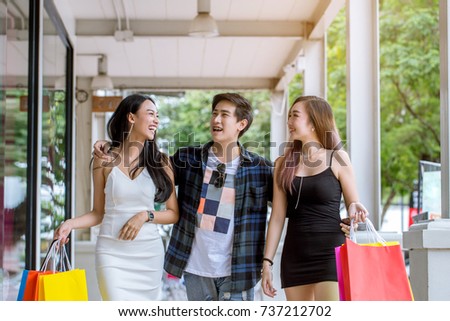 Two Beautiful Asian women and Asian playboy are shopping happily during the daytime.