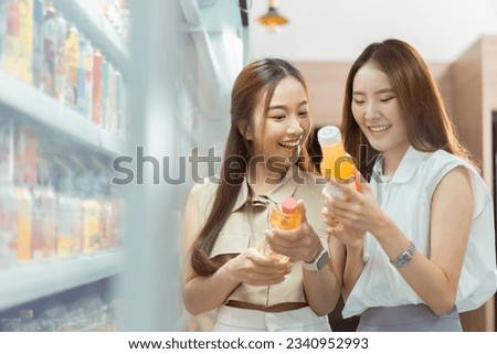 Two beautiful Asian women shopping and checking items in supermarket. Female friends meeting and examining nutrition labels at convenient store