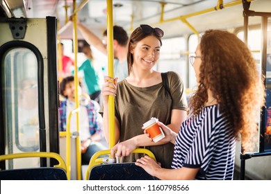 Two Beautiful Best Friends Are Talking While Standing In A Bus Full Of People.