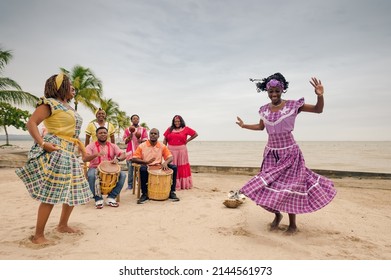 Two beautiful black women dance on a Caribbean beach, accompanied by a local musical group.