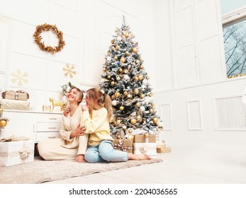 Two Beautiful Blond Women. Models Posing Near Decorated Christmas Tree At New Year Eve. Having Fun, Ready For Celebration. Bright Holiday Of Best Friends Dressed In Warm Winter Sweaters