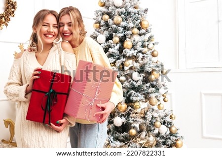 Two beautiful blond women. Models posing near decorated Christmas tree at New Year eve. Having fun, ready for celebration. Bright holiday of best friends dressed in warm winter sweaters