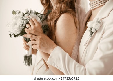 Two beautiful brides in white attire during their wedding ceremony, holding hands and a bouquet of flowers. - Powered by Shutterstock