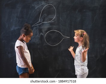 Two Beautiful Elementary School Girls Standing In Front Of A Chalkboard In Classroom, Having A Discussion And Debate