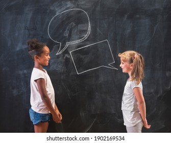 Two beautiful elementary school girls standing in front of a chalkboard in classroom, having a discussion and debate - Shutterstock ID 1902169534