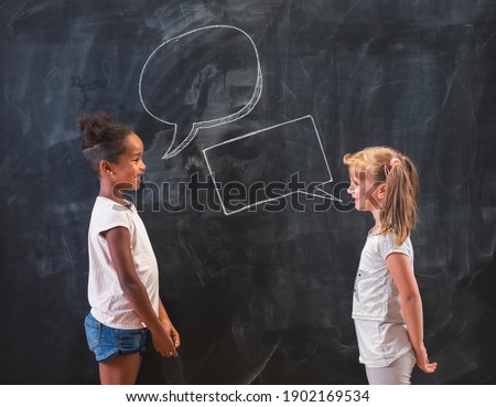Two beautiful elementary school girls standing in front of a chalkboard in classroom, having a discussion and debate