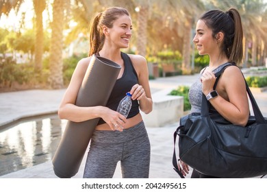 Two beautiful fitness female friends in sportswear holding gym bag, yoga mat and water bottle talking in the park. Sporty girl ready for training. - Powered by Shutterstock