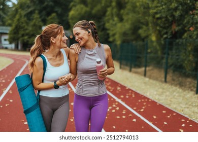 Two beautiful fitness female friends in sportswear holding gym bag, yoga mat and water bottle talking in the park. Sporty girl ready for training. Two female friends spending time together - Powered by Shutterstock